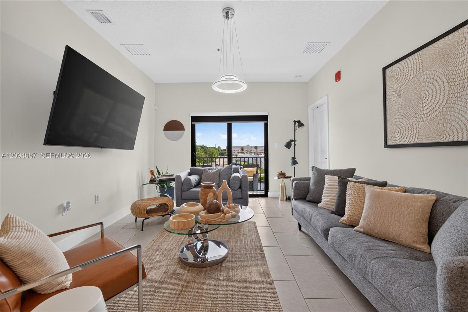 Staged living room with gray sofas, a glass coffee table, and sliding doors to a balcony.