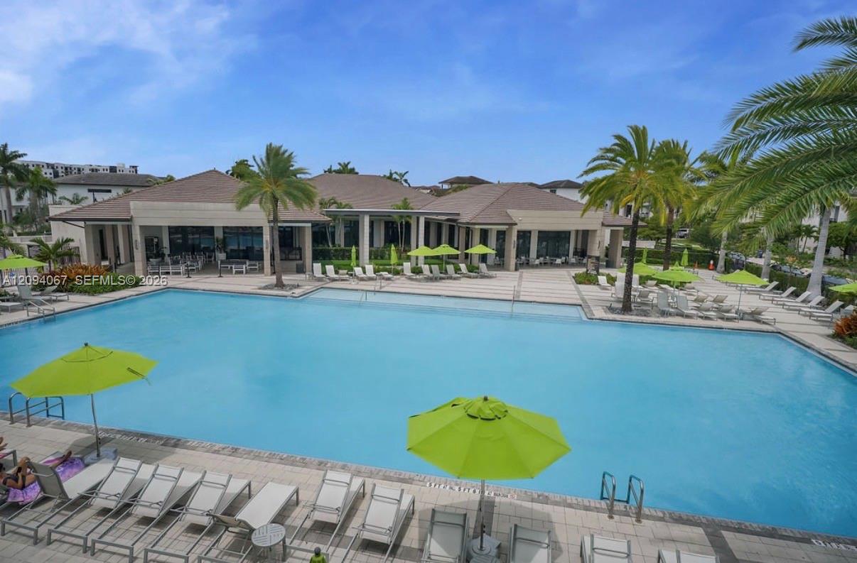 Community swimming pool with lime-green umbrellas, lounge chairs, palm trees, and a clubhouse.
