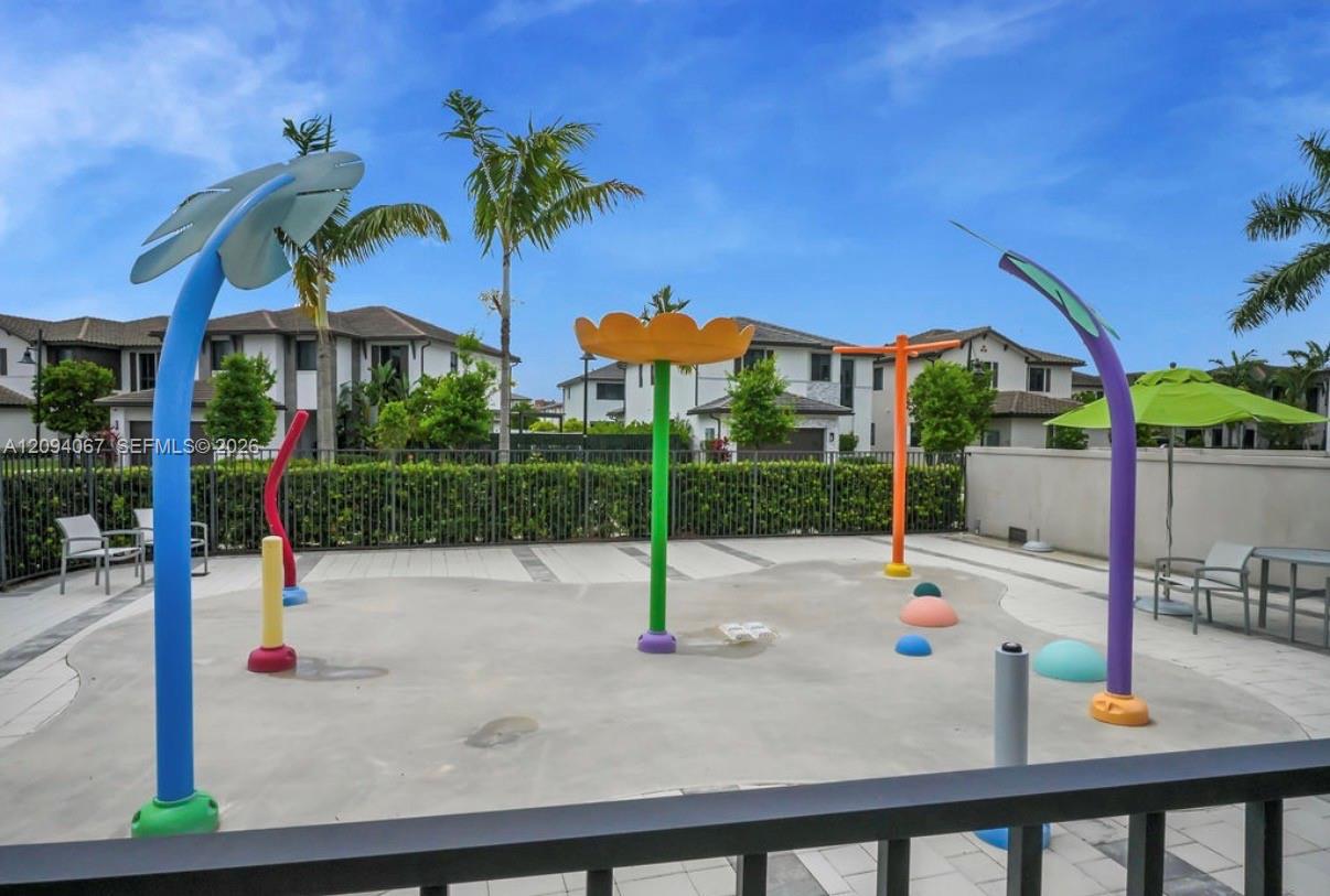 Community splash pad with colorful water features, patio seating, and palm trees.