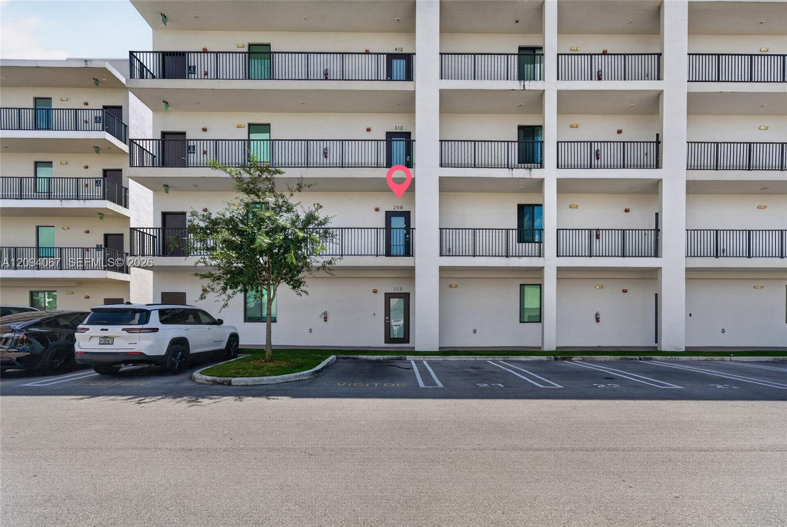 Apartment building exterior with black-railed balconies; a pink marker identifies unit 208 above the parking area.