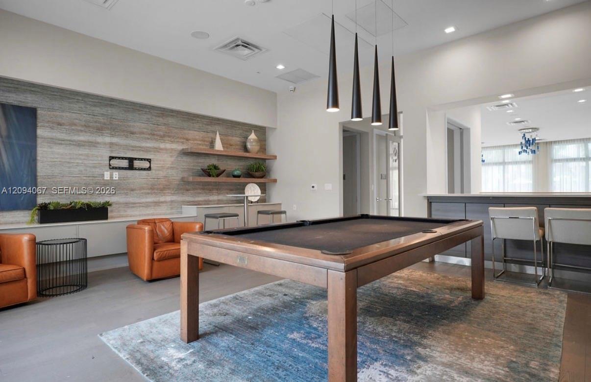 Game room with a billiards table, leather lounge chairs, and bar seating.