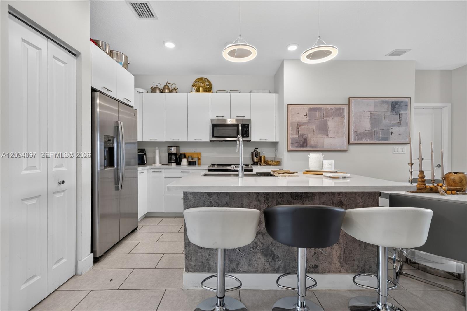 Modern kitchen with white cabinets, stainless steel appliances, and a large island with three bar stools.