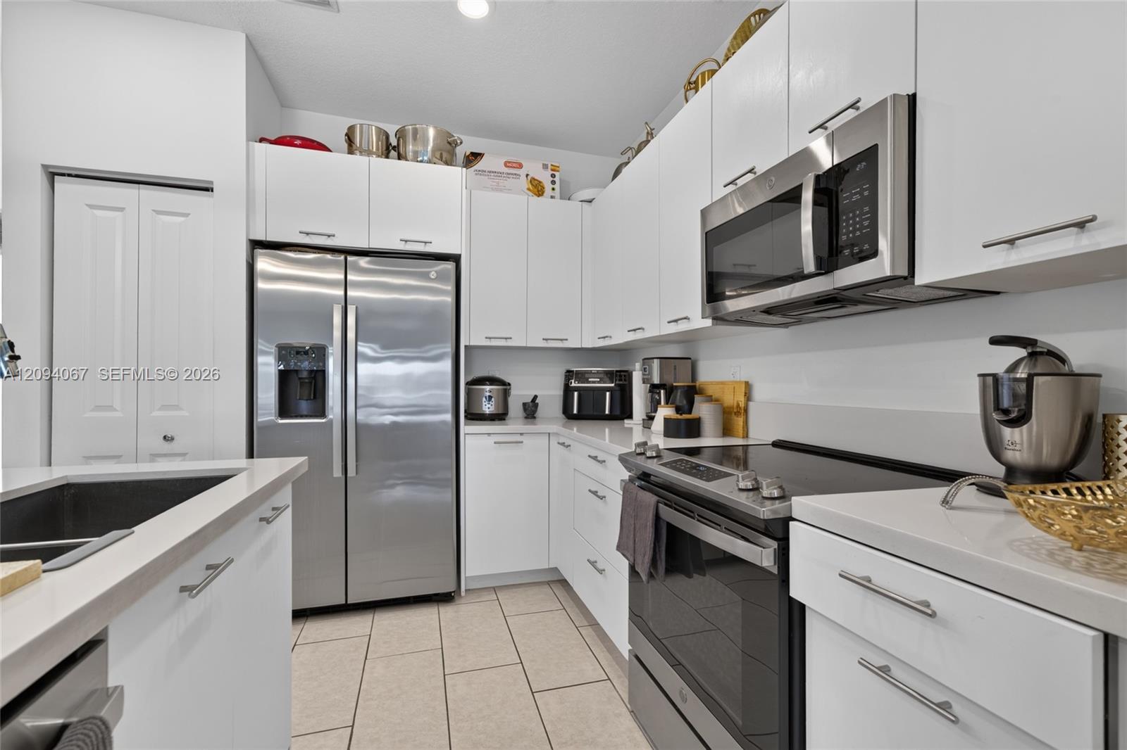 Compact white kitchen with stainless steel appliances, tiled floor, and cookware on the counters.