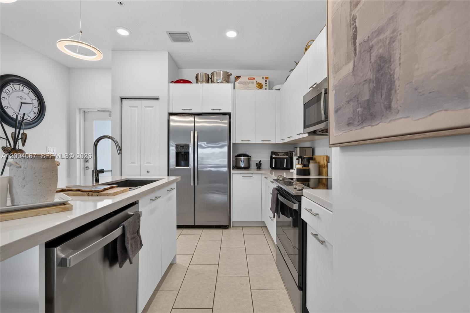 Modern white kitchen with stainless-steel appliances, a peninsula sink, and light tile flooring.