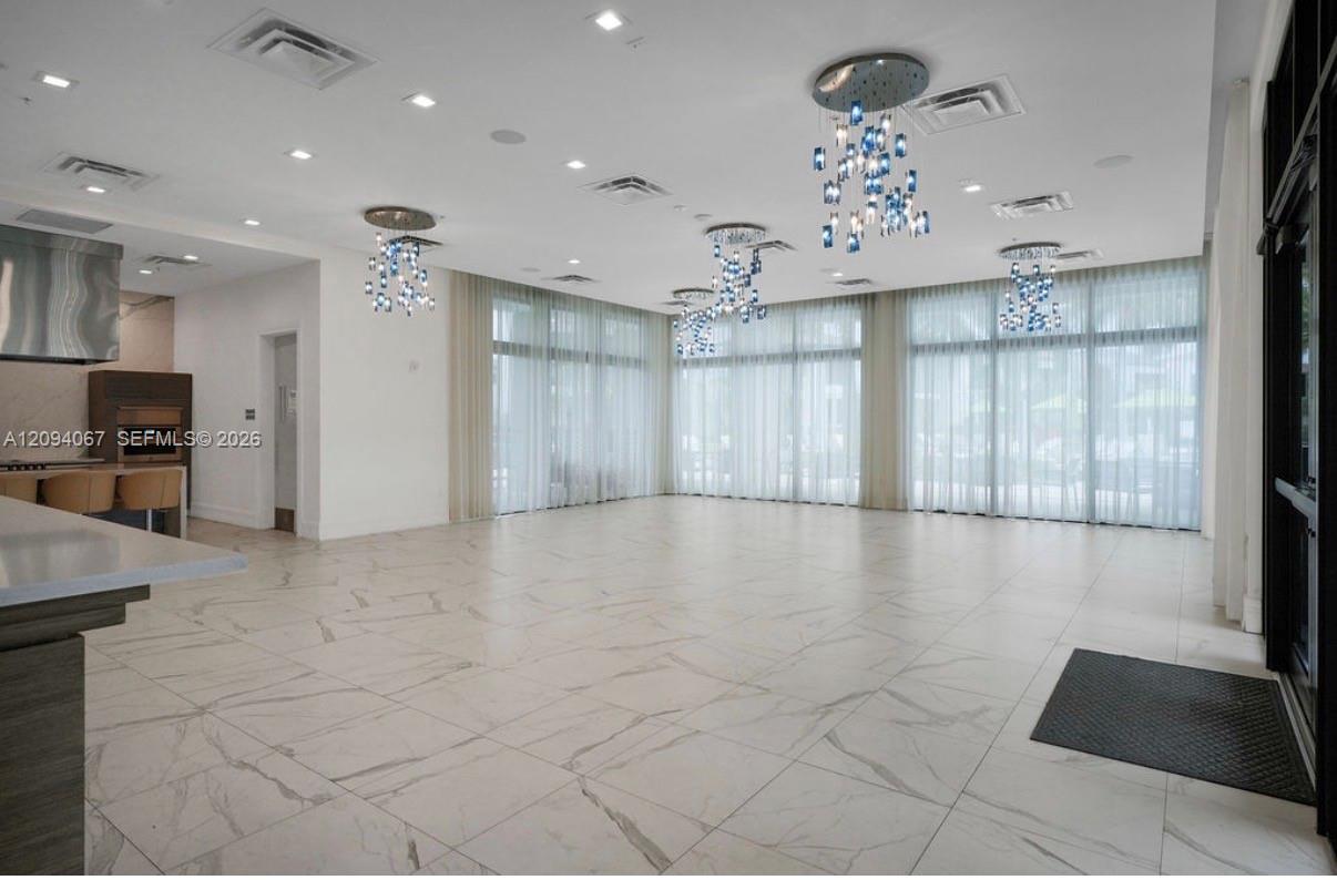 Vacant open living and dining area with marble-pattern floors, sheer-curtained windows, and crystal chandeliers.
