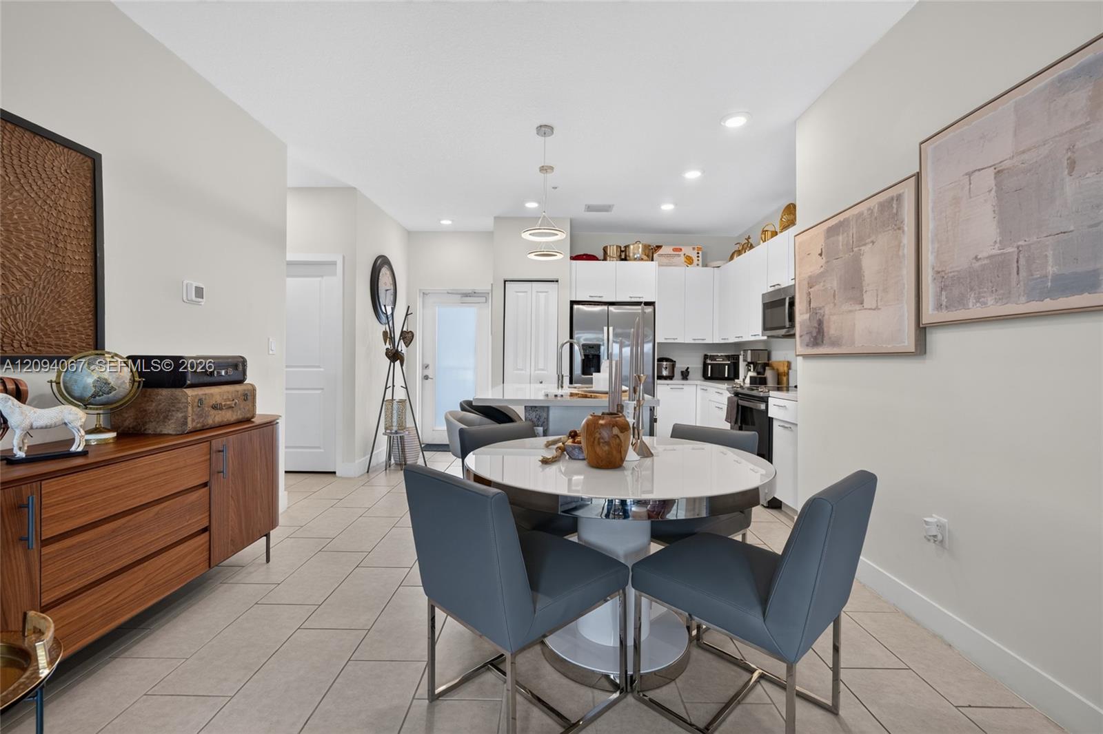Open-plan kitchen and dining area with white cabinets, stainless steel appliances, and a round table with blue-gray chairs.