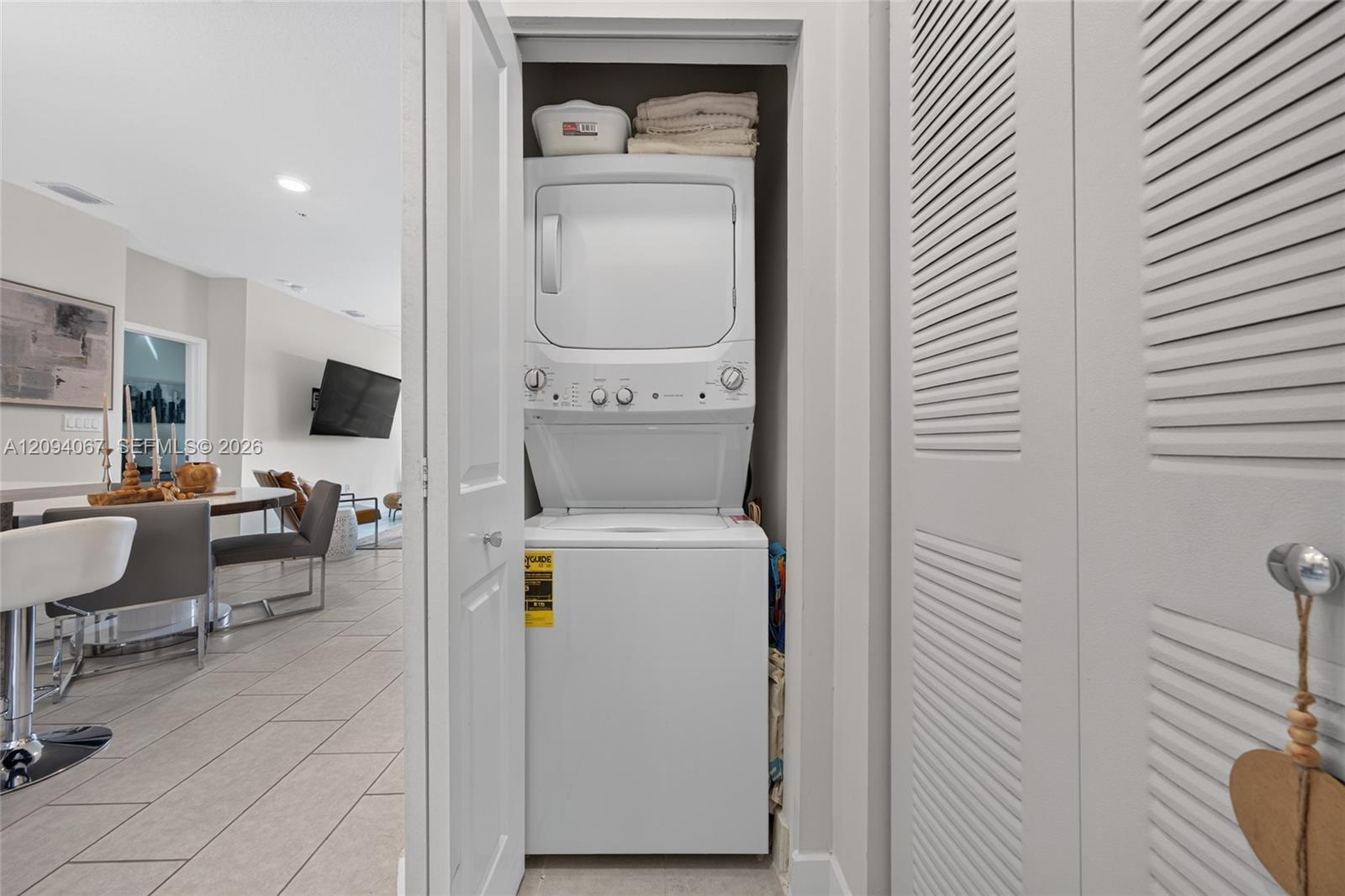 Stacked washer and dryer in a closet beside the furnished dining and living area.