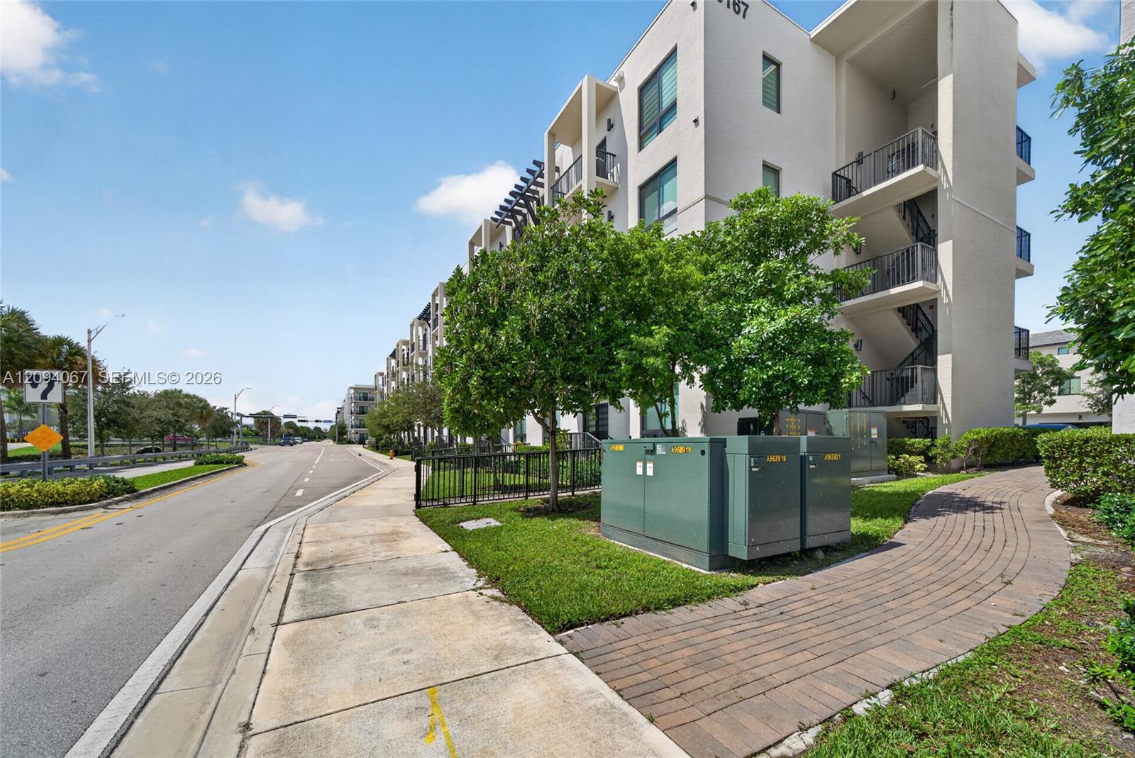 Modern multi-story residential building with stacked balconies and a curved brick-paver walkway.