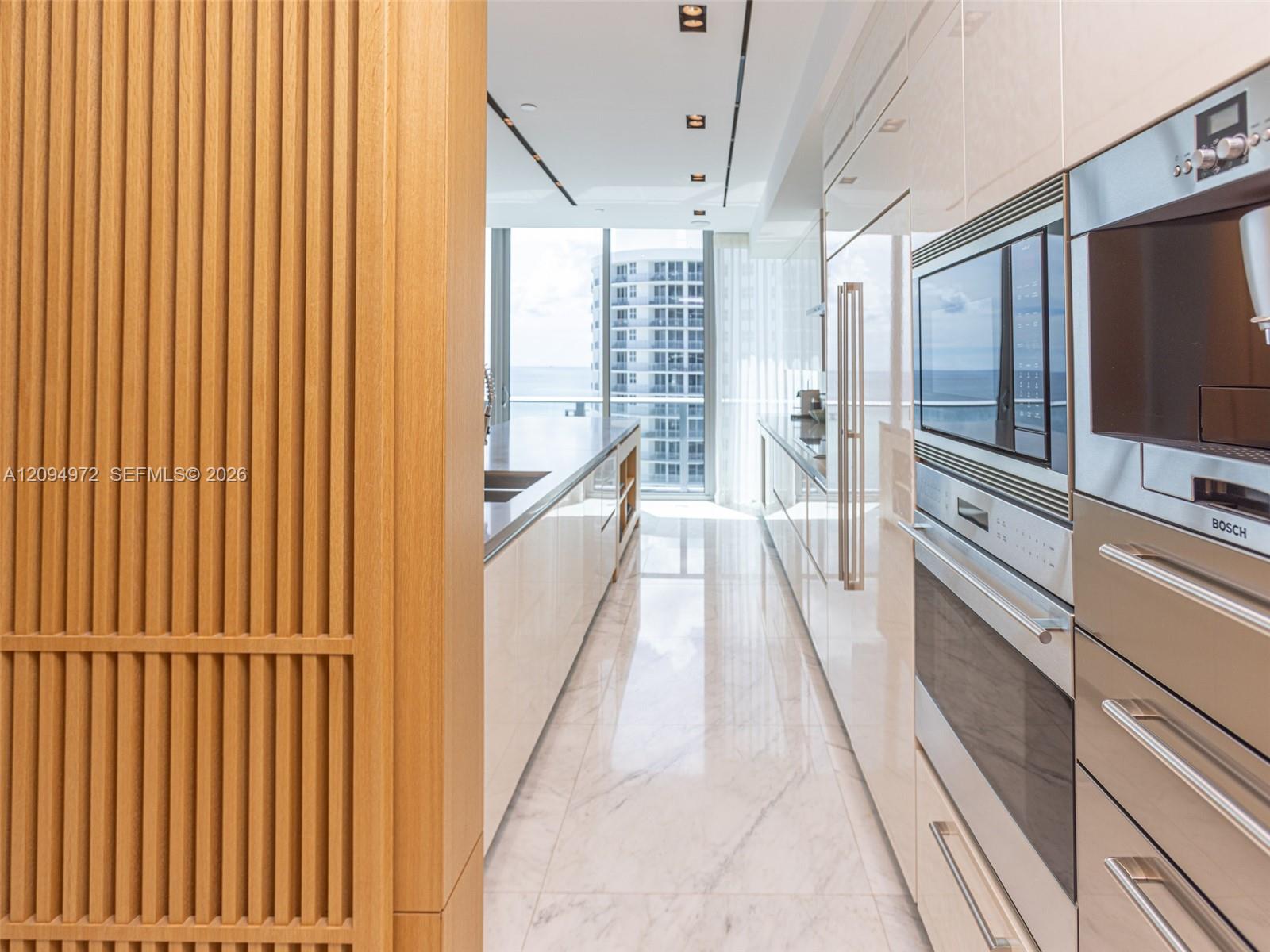 Modern galley kitchen with built-in stainless steel appliances and ocean views through the windows.