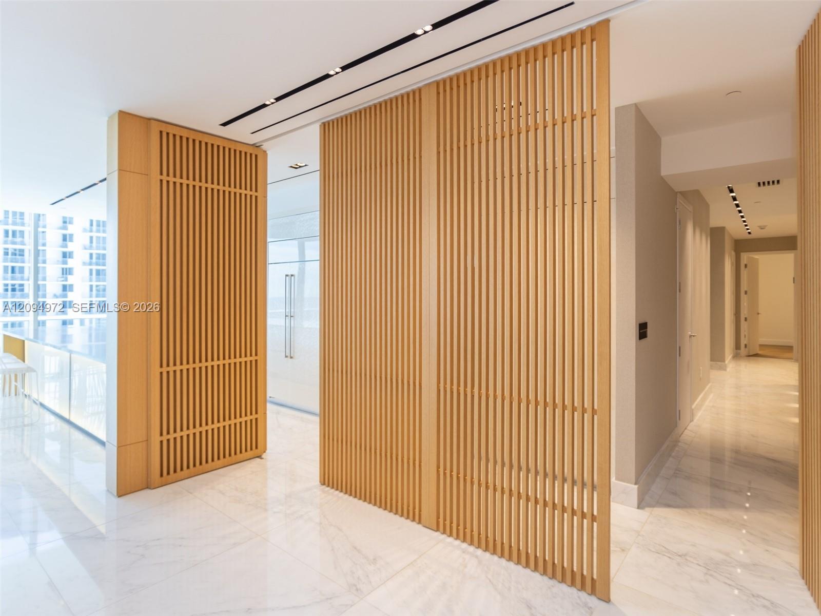 Bright condo foyer with wood slat screens, polished marble flooring, and a long hallway.