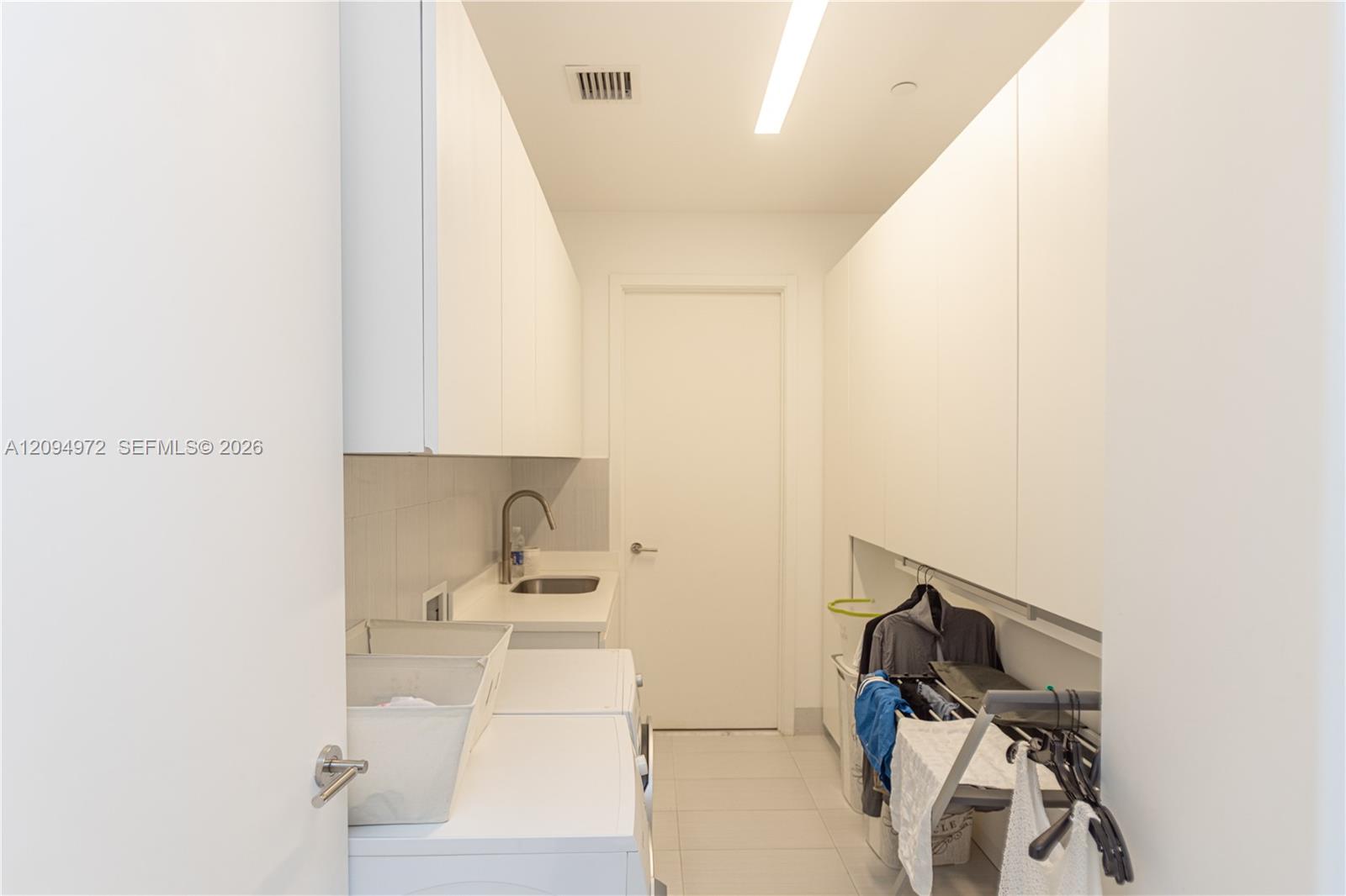 Laundry room with white built-in cabinets, washer and dryer, utility sink, and hanging clothes.