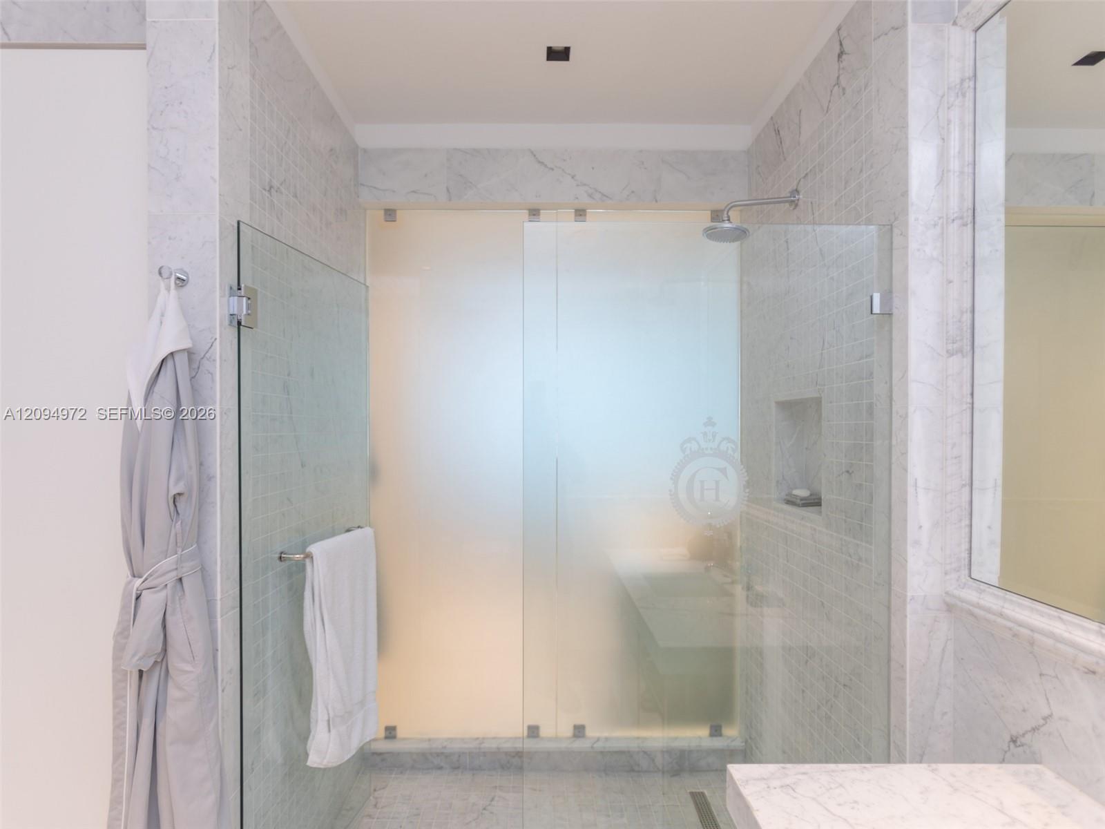 Marble bathroom with a glass-enclosed shower, rain showerhead, recessed niche, and hanging towels.