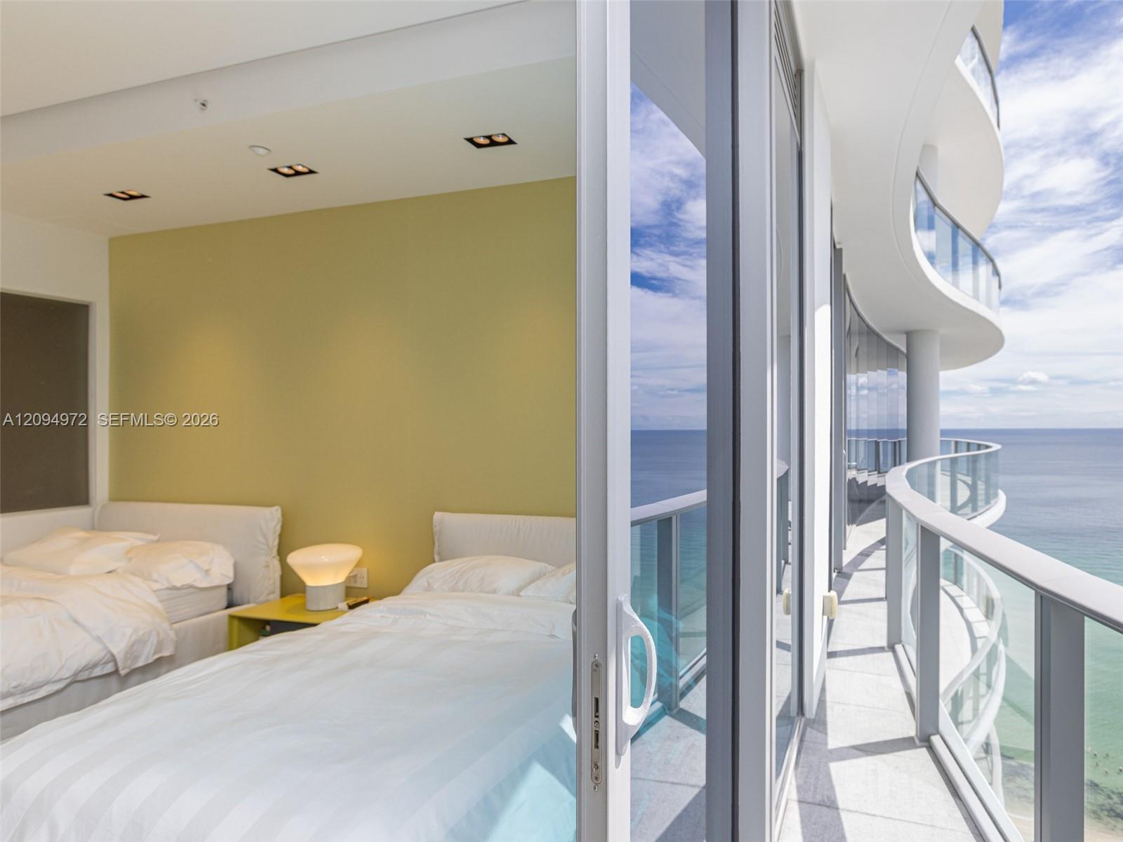 Furnished bedroom opens onto a curved oceanfront balcony with glass railings.