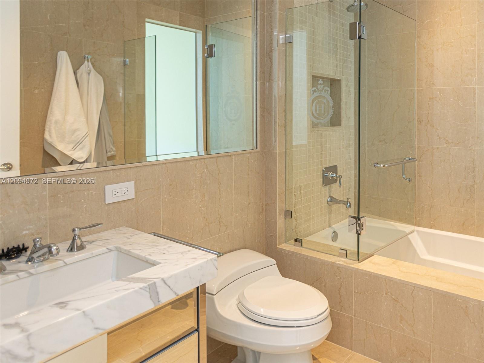 Marble bathroom with a glass-enclosed tub and shower, white toilet, and marble vanity.