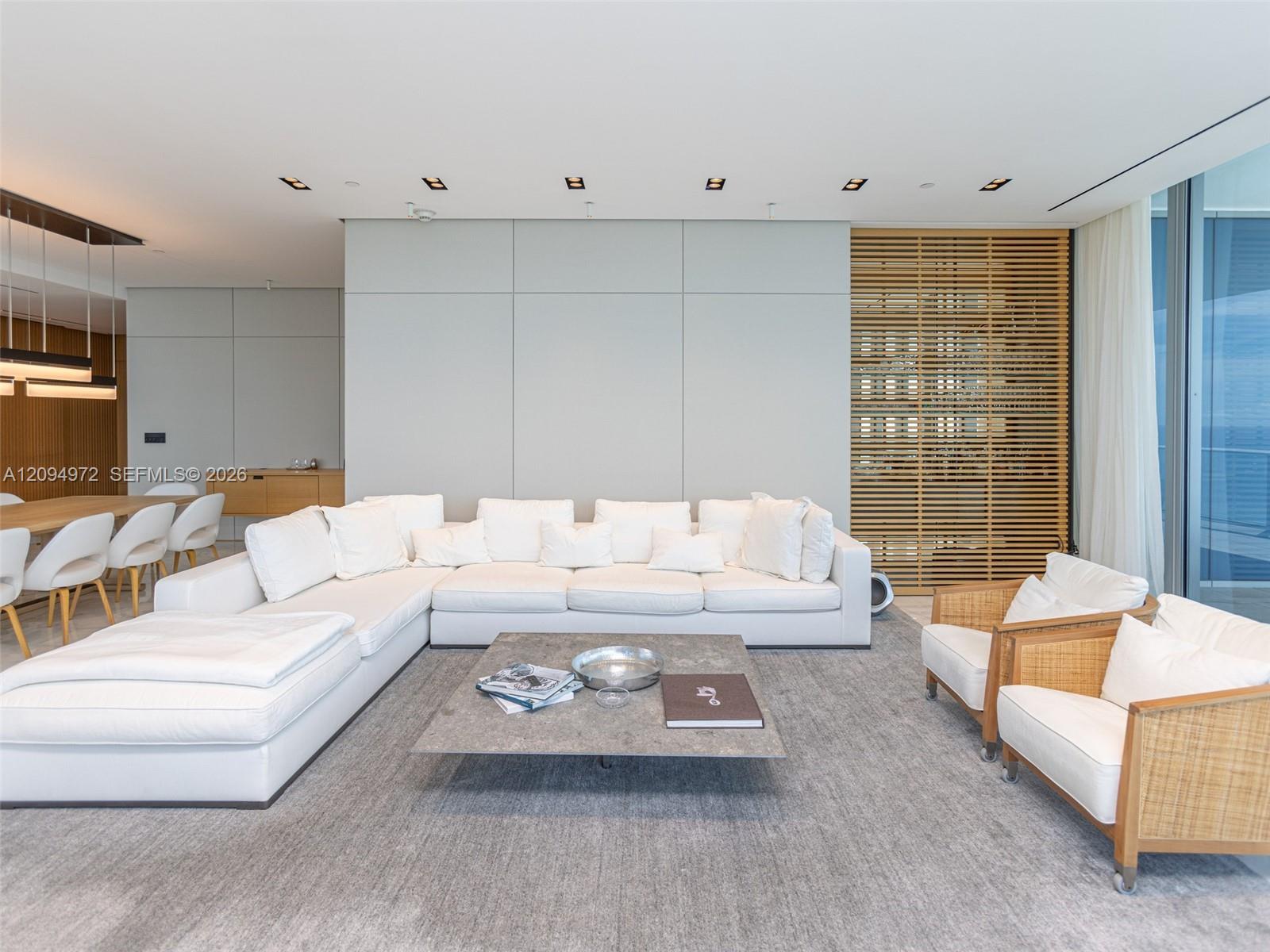 Modern condo living room with a large white sectional, woven chairs, and floor-to-ceiling windows.