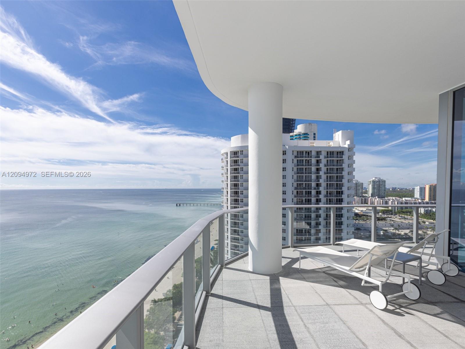 High-rise balcony with white loungers overlooking the ocean, beach, and neighboring towers.