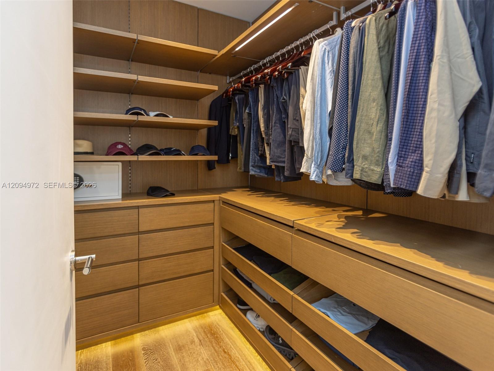 Walk-in closet with warm wood cabinetry, hanging clothes, and built-in shoe shelves.
