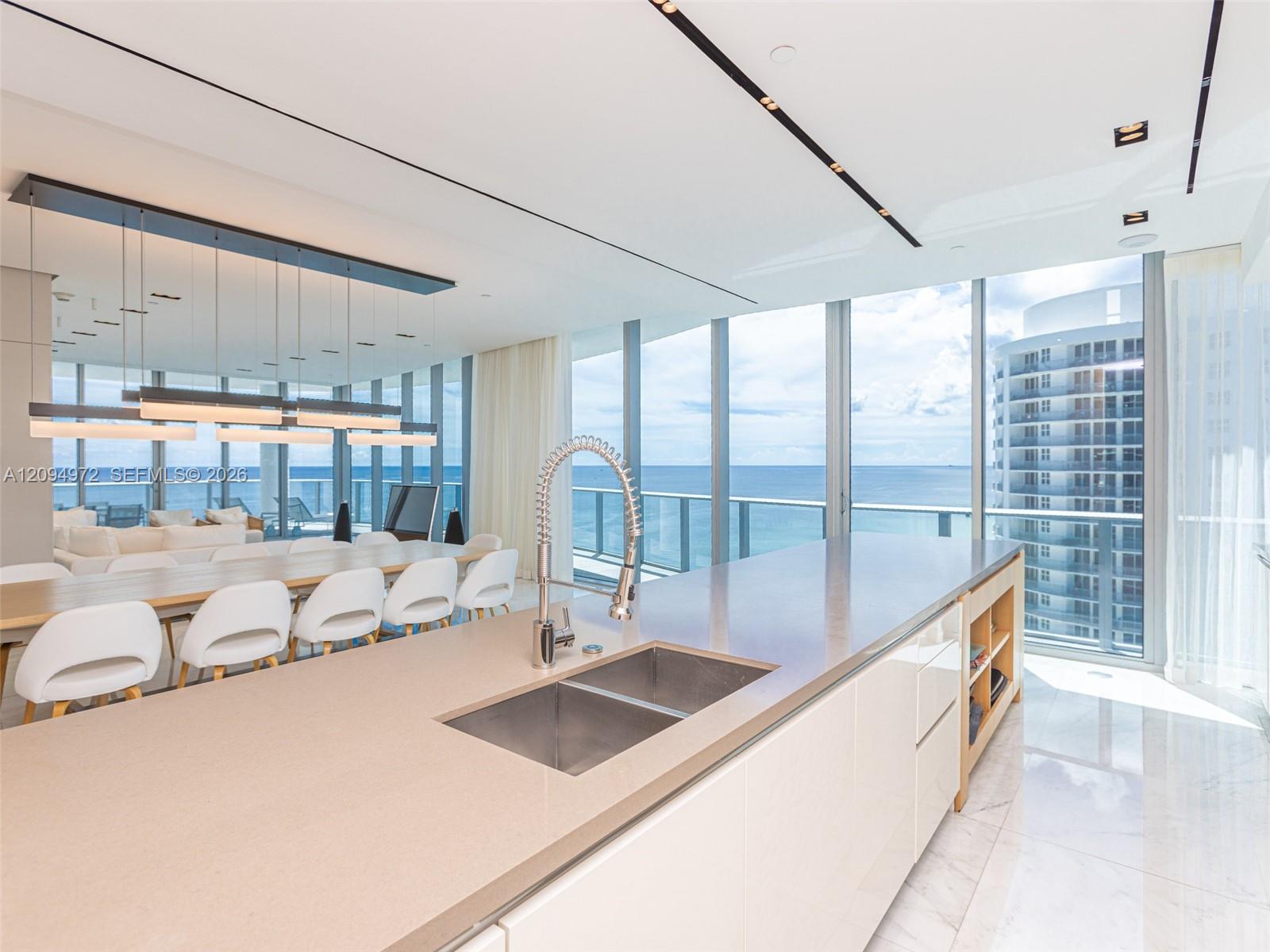 Modern kitchen with a large island and dining area overlooking the ocean through floor-to-ceiling windows.