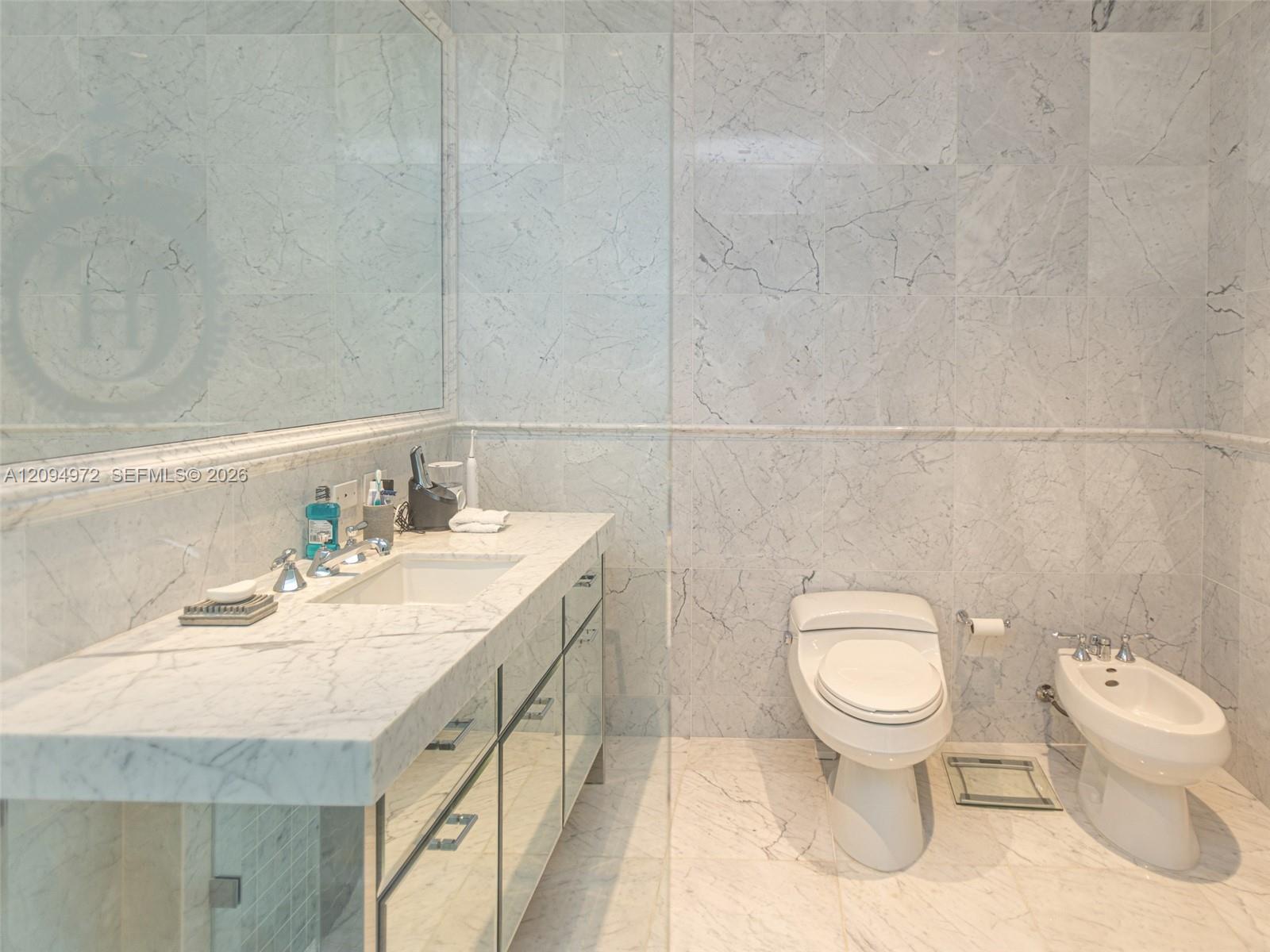 Marble bathroom with a long vanity, large mirror, toilet, and bidet.