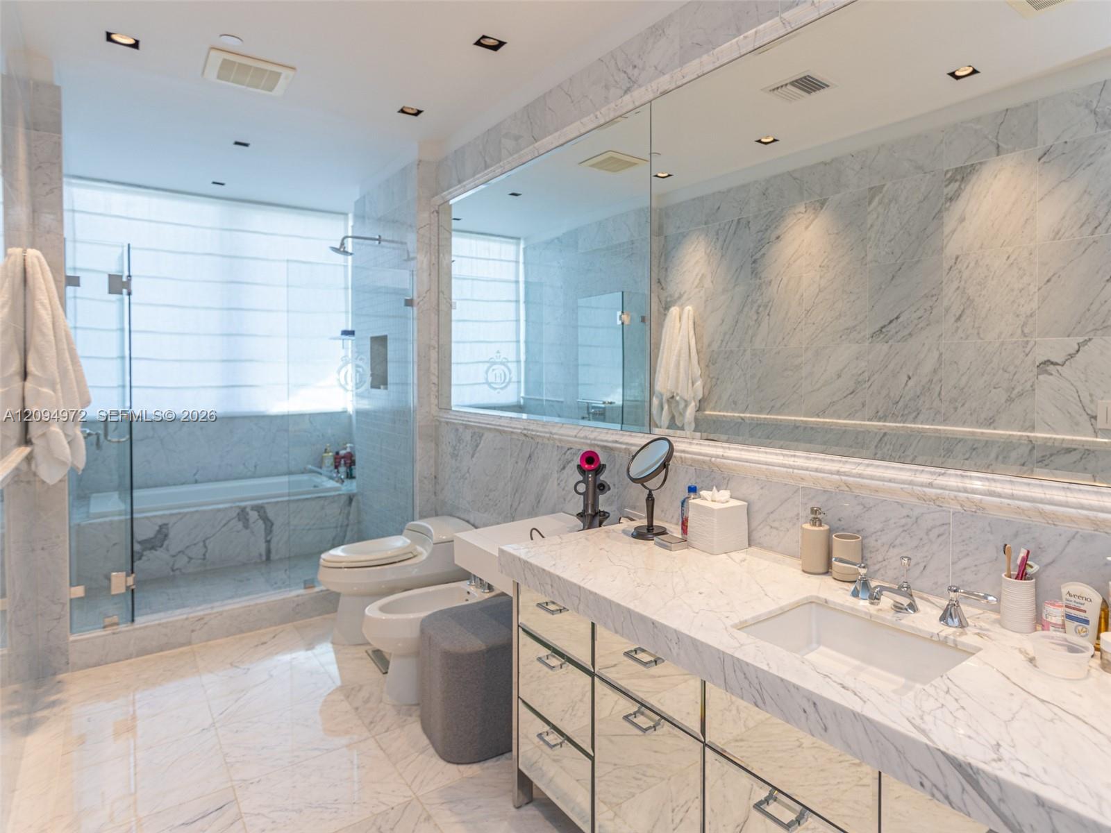 Marble bathroom with a glass shower, bathtub, and large mirrored vanity.