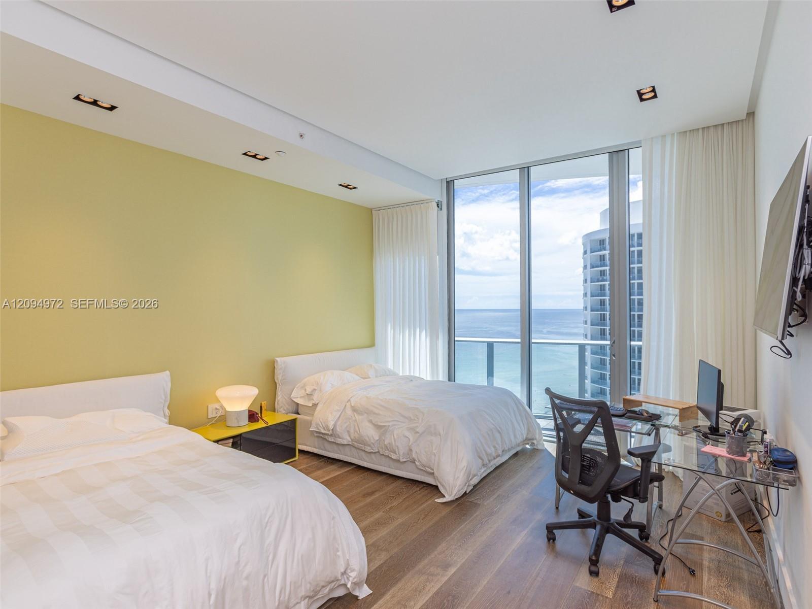Bedroom with two beds and floor-to-ceiling windows overlooking the ocean.