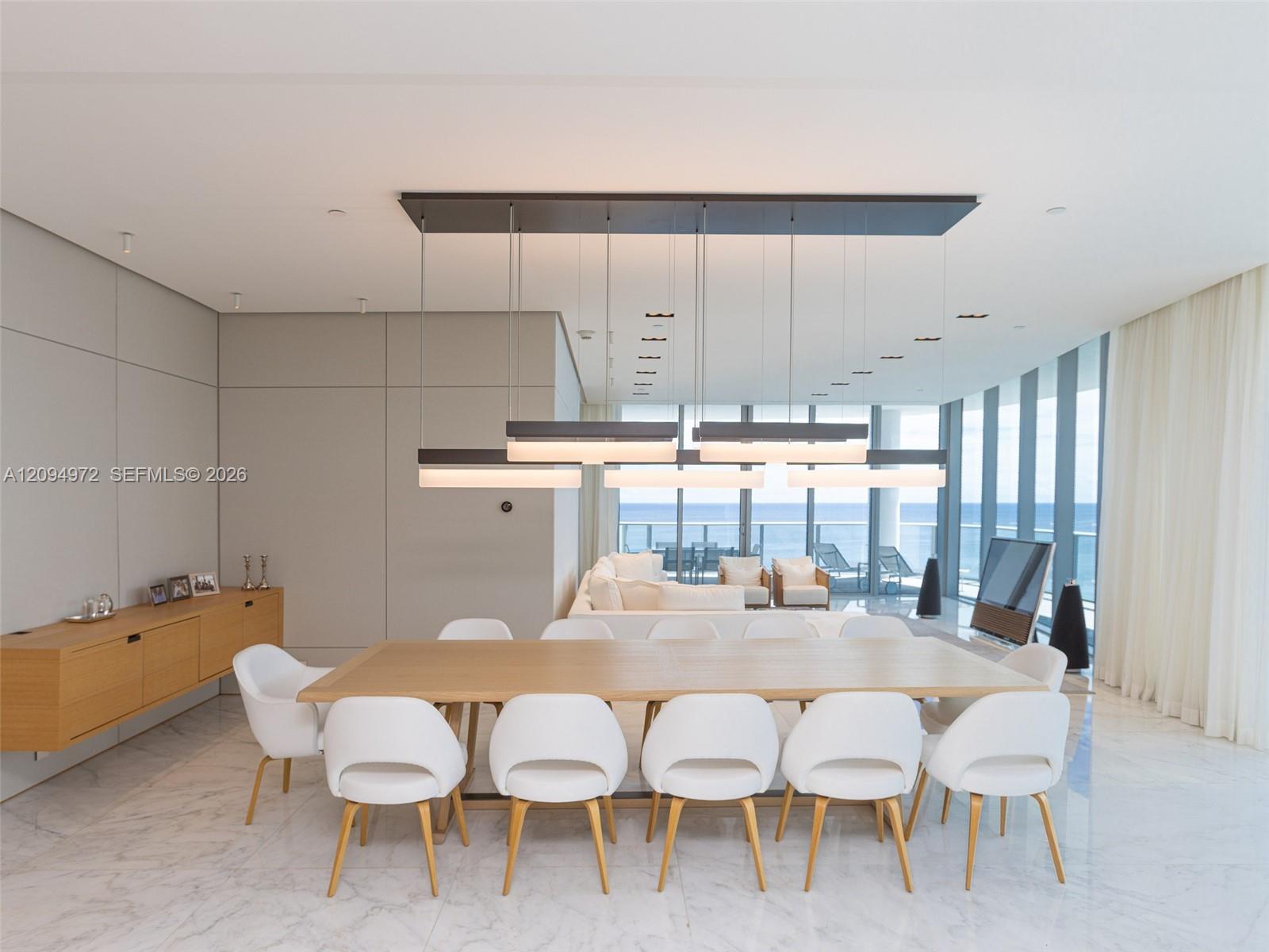 Modern dining room with a long wood table and white chairs overlooking the ocean.