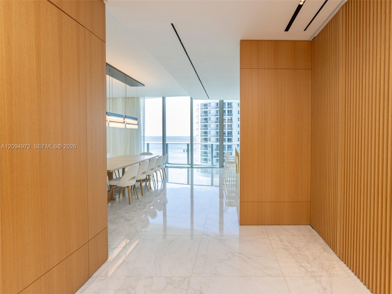 Wood-paneled entry opens to a dining area with floor-to-ceiling windows overlooking the water.