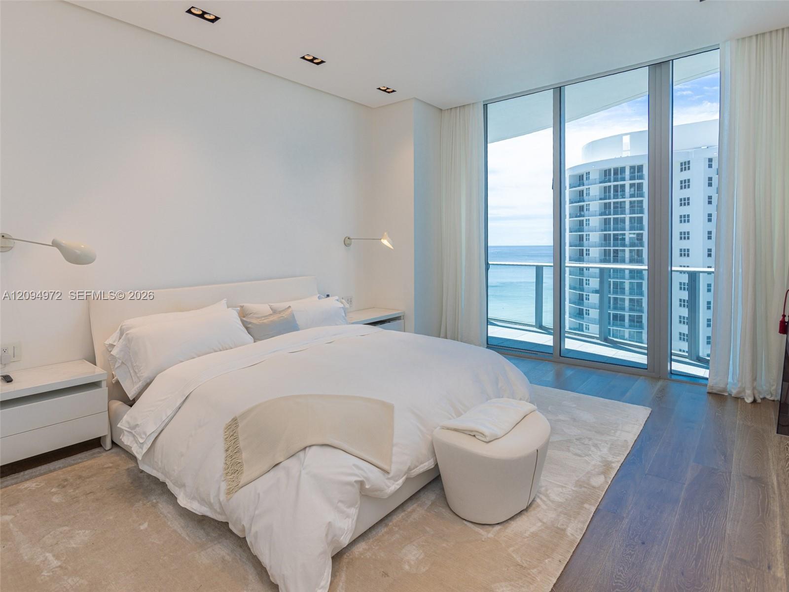 Modern condo bedroom with a white bed and floor-to-ceiling ocean-view windows.