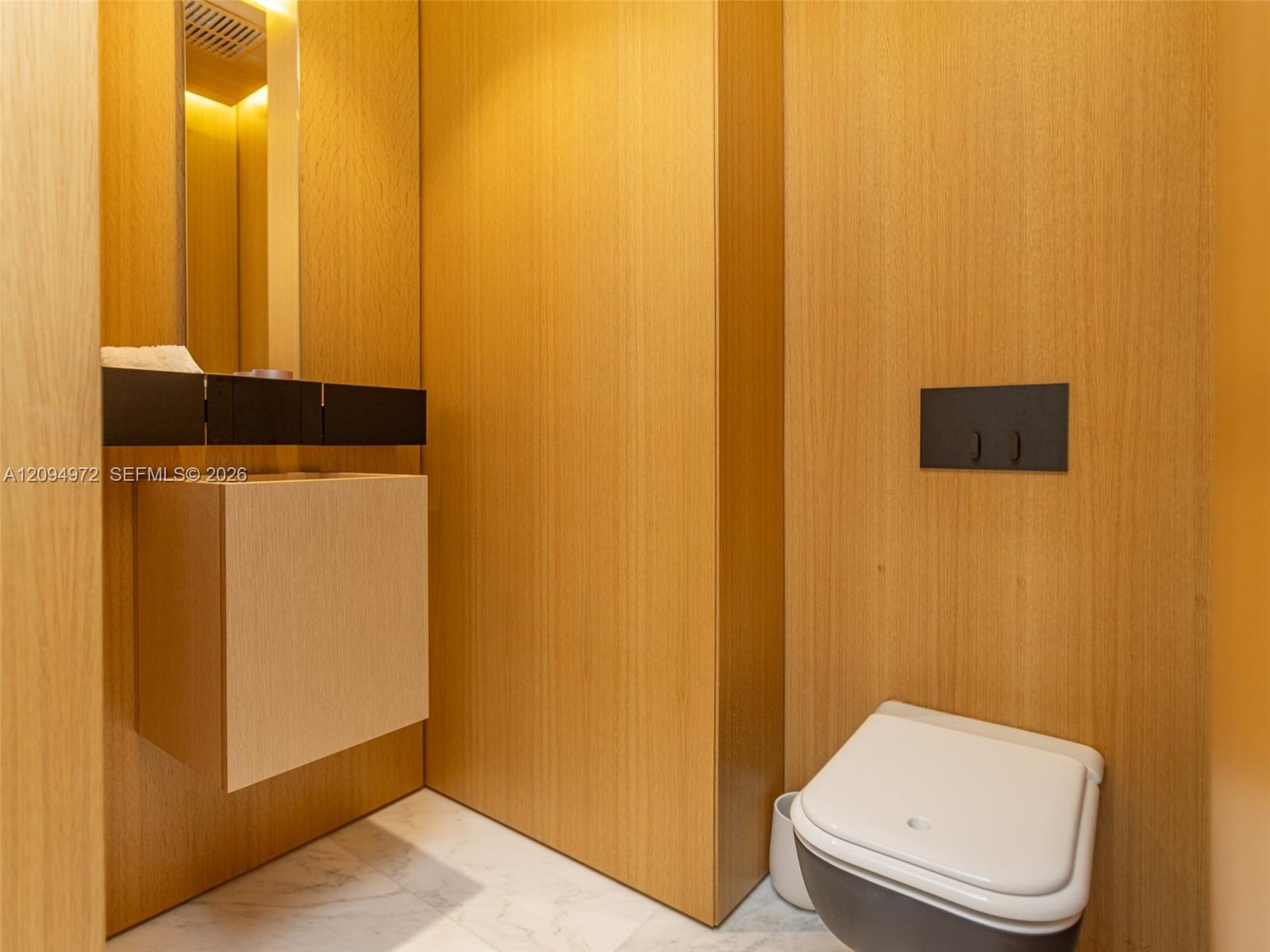 Contemporary bathroom with a wall-mounted toilet, floating vanity, and warm wood-paneled walls.