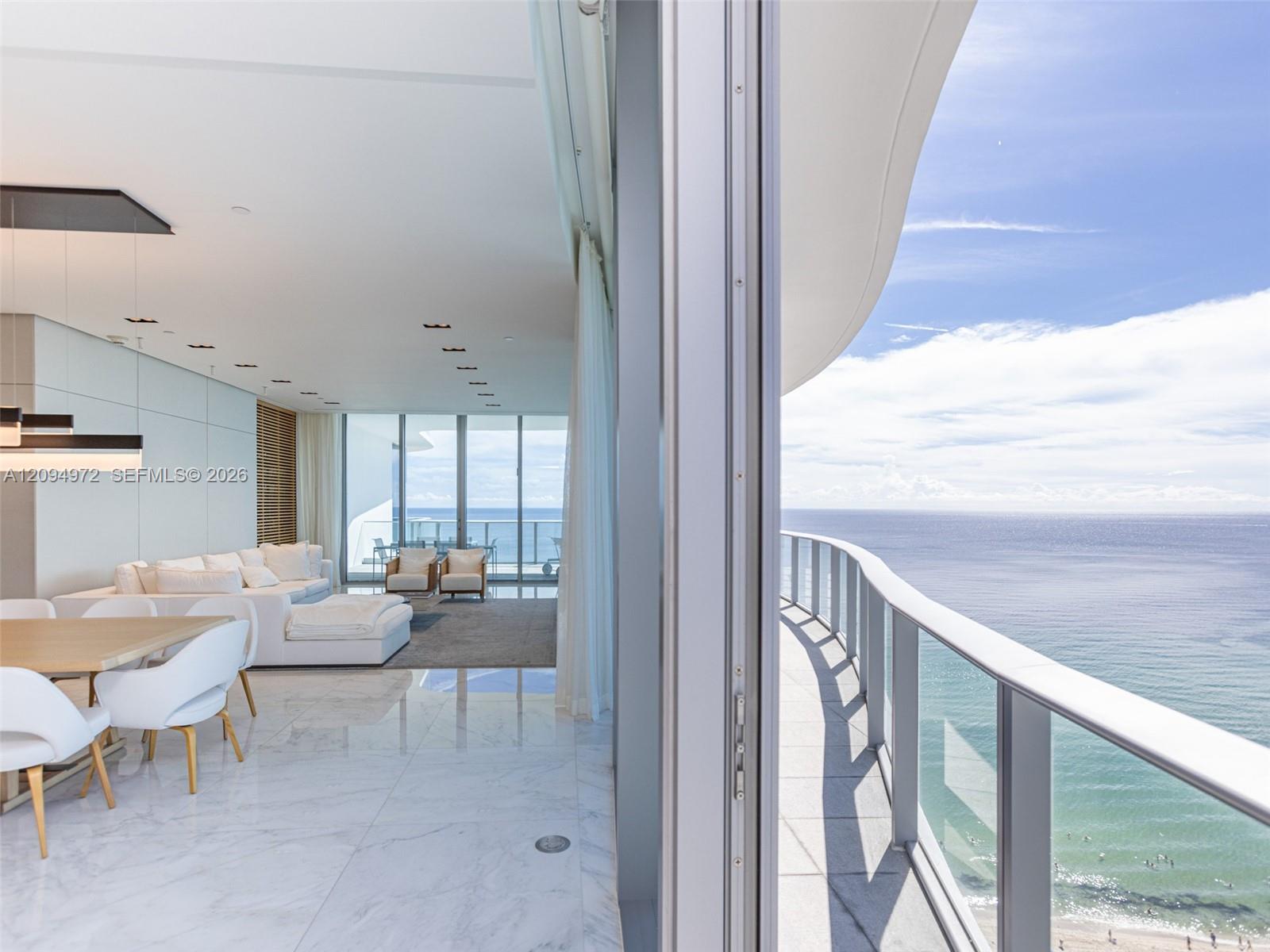 Furnished condo living and dining area opening to a curved ocean-view balcony.