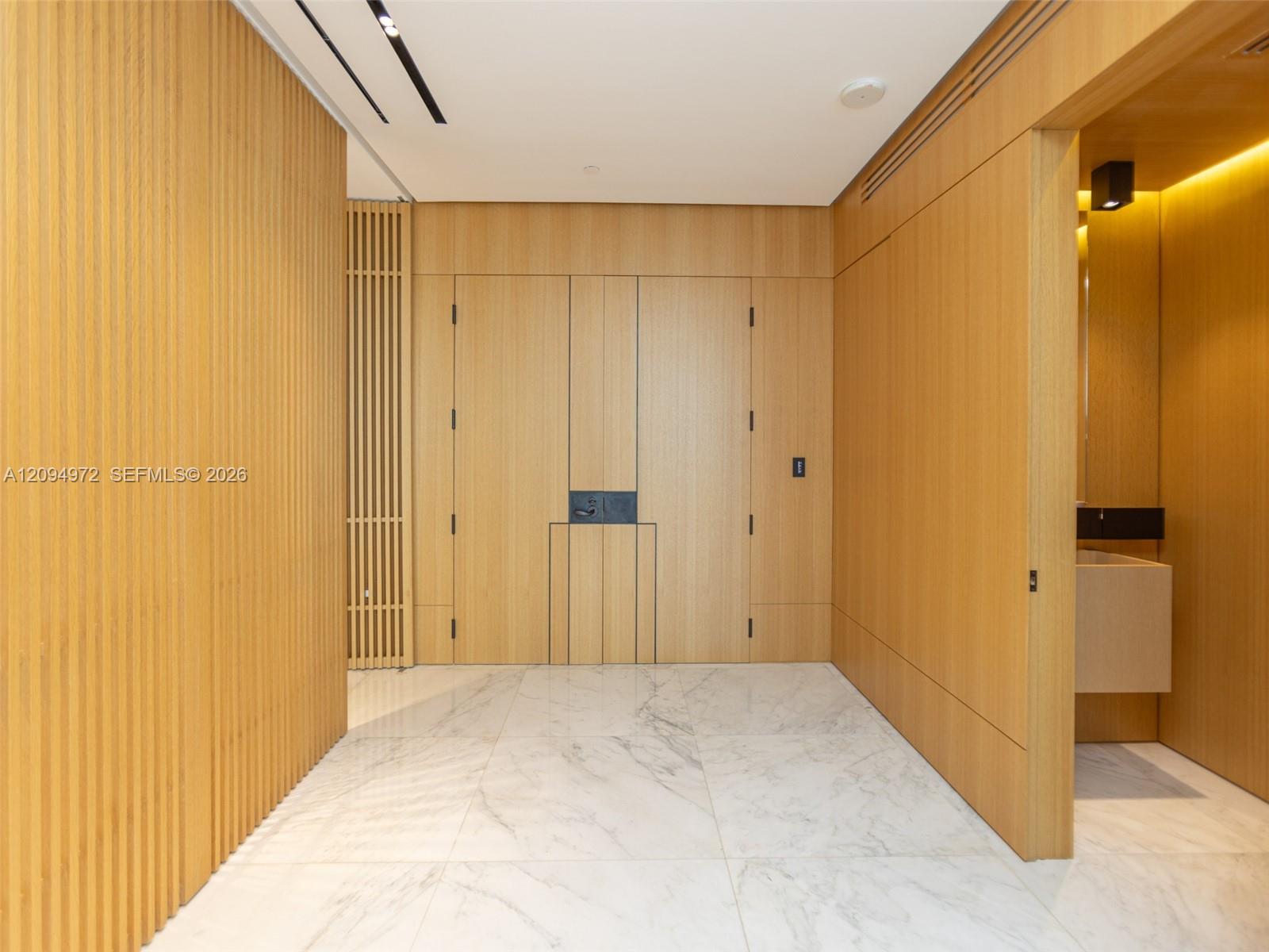 Condo foyer with warm wood paneling, concealed doors, and a white veined marble floor.