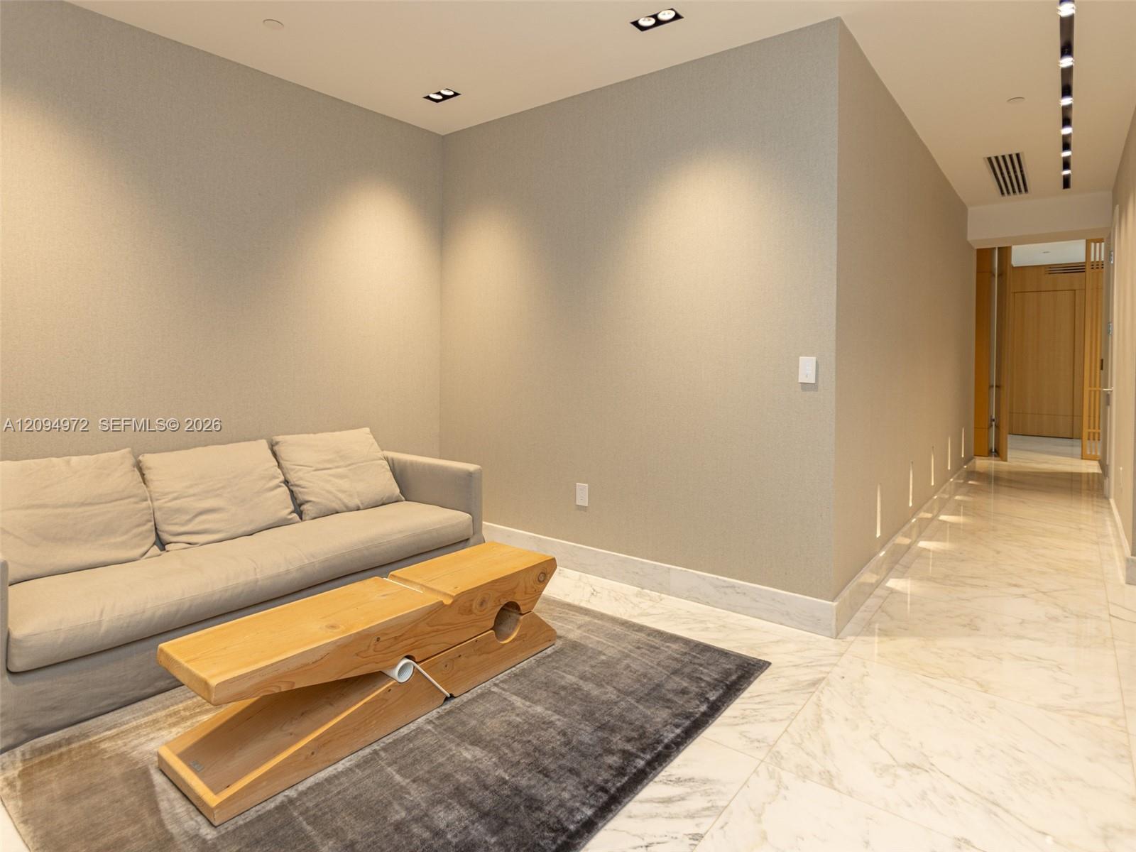 Living room with a gray sofa, sculptural wooden coffee table, and marble flooring.