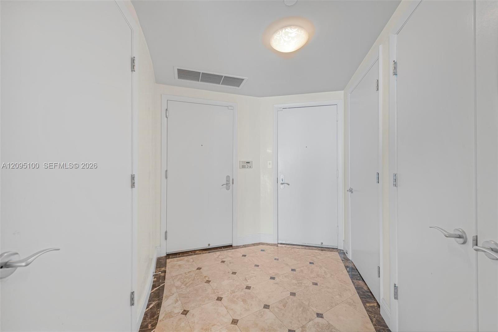Entry foyer with multiple white doors and patterned marble tile flooring.