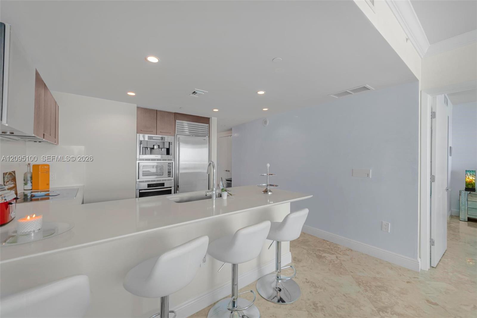 Modern condo kitchen with a long white island, bar stools, and stainless steel appliances.