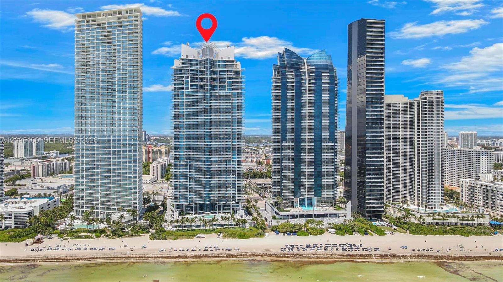 Beachfront high-rise condominium tower marked by a red pin, with neighboring towers and shoreline.