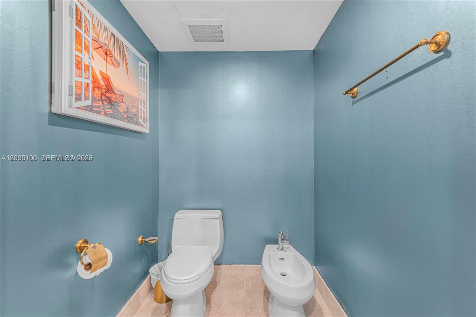 Bathroom with teal walls, white toilet and bidet, and gold-tone fixtures.
