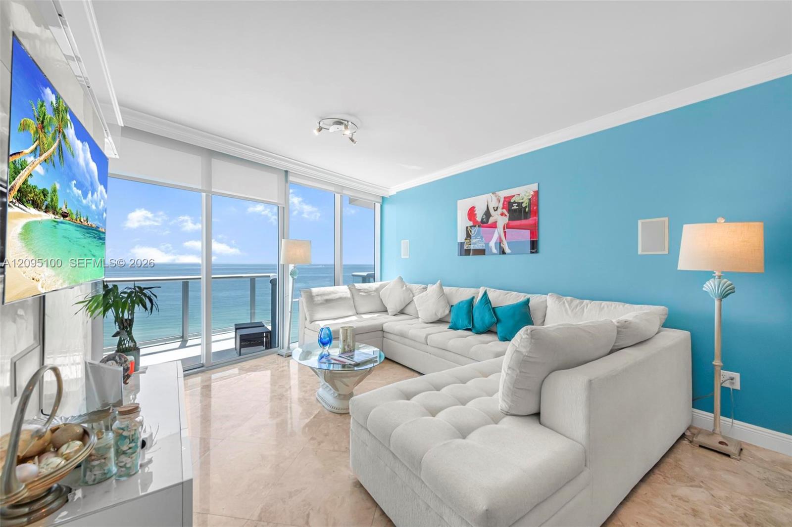 Living room with a white sectional and turquoise wall, facing floor-to-ceiling ocean-view windows.