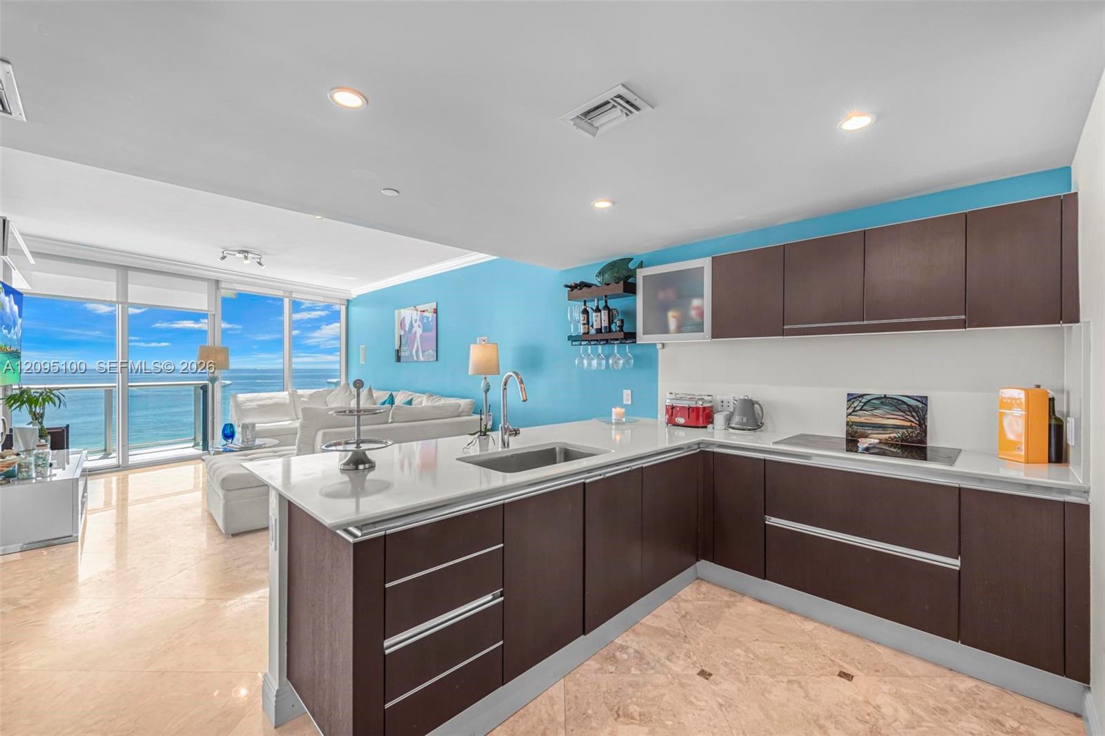 Open-plan condo kitchen with dark cabinetry and ocean views through floor-to-ceiling living room windows.