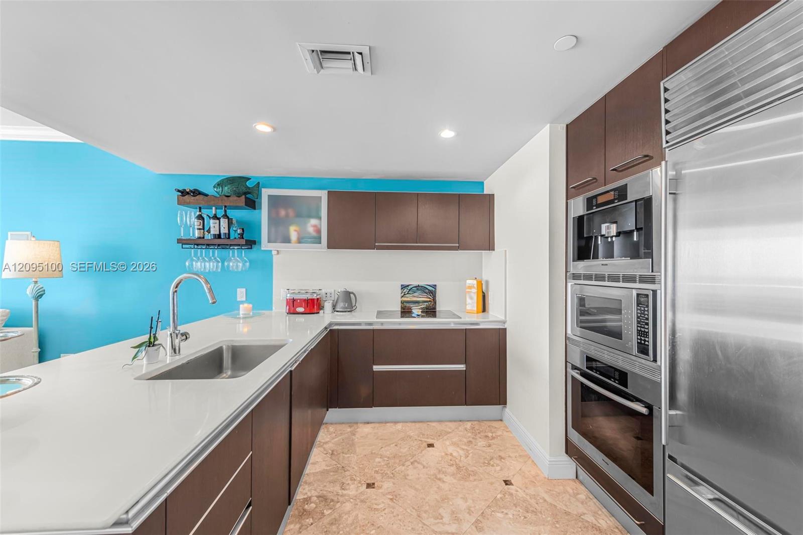 Modern condo kitchen with dark wood cabinetry, stainless appliances, white counters, and turquoise accent wall.