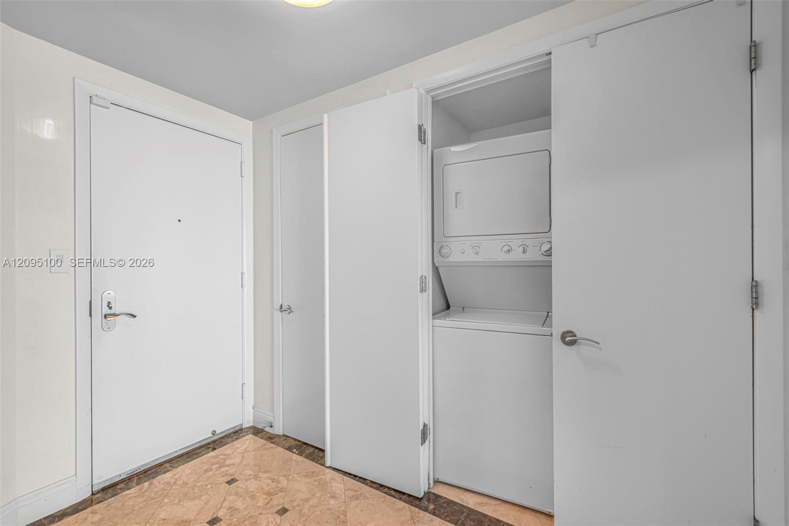 Condo entryway with marble tile flooring and an open closet with a stacked washer and dryer.