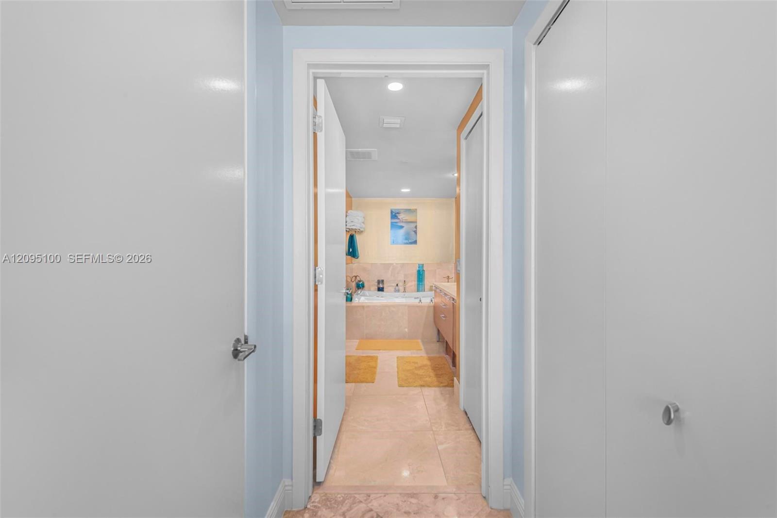 Bathroom viewed through an open doorway, with a bathtub, vanity, and yellow bath rugs.