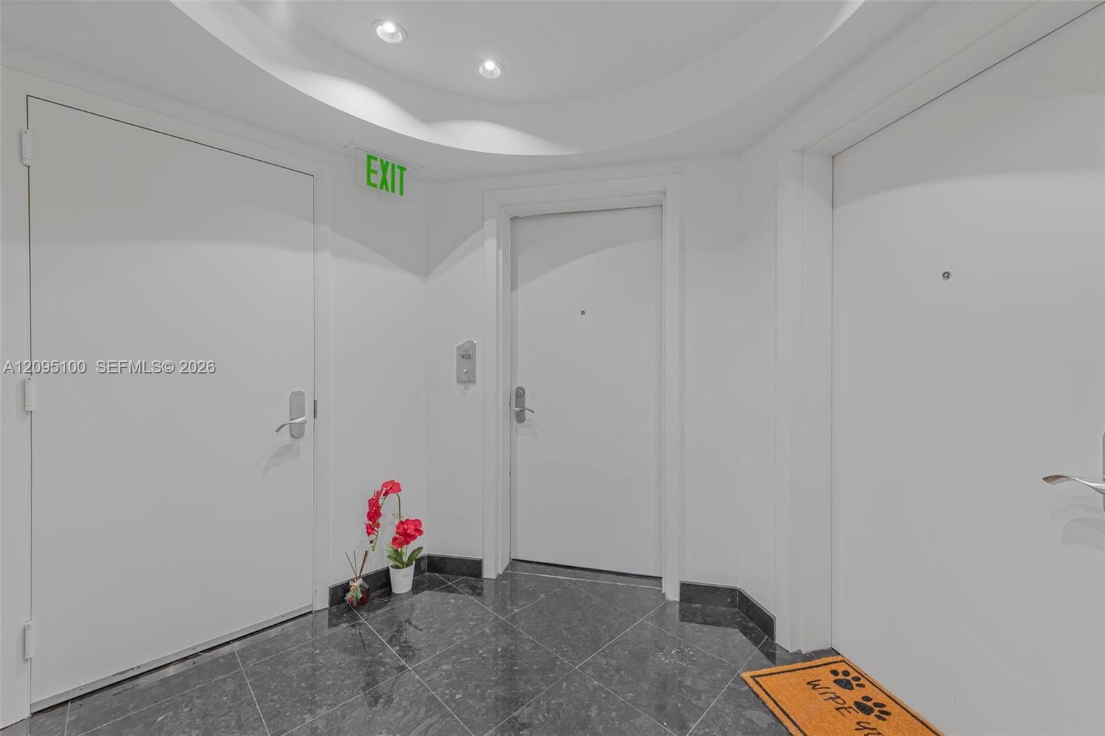 Condominium entry foyer with gray marble flooring, white doors, red flowers, and an EXIT sign.