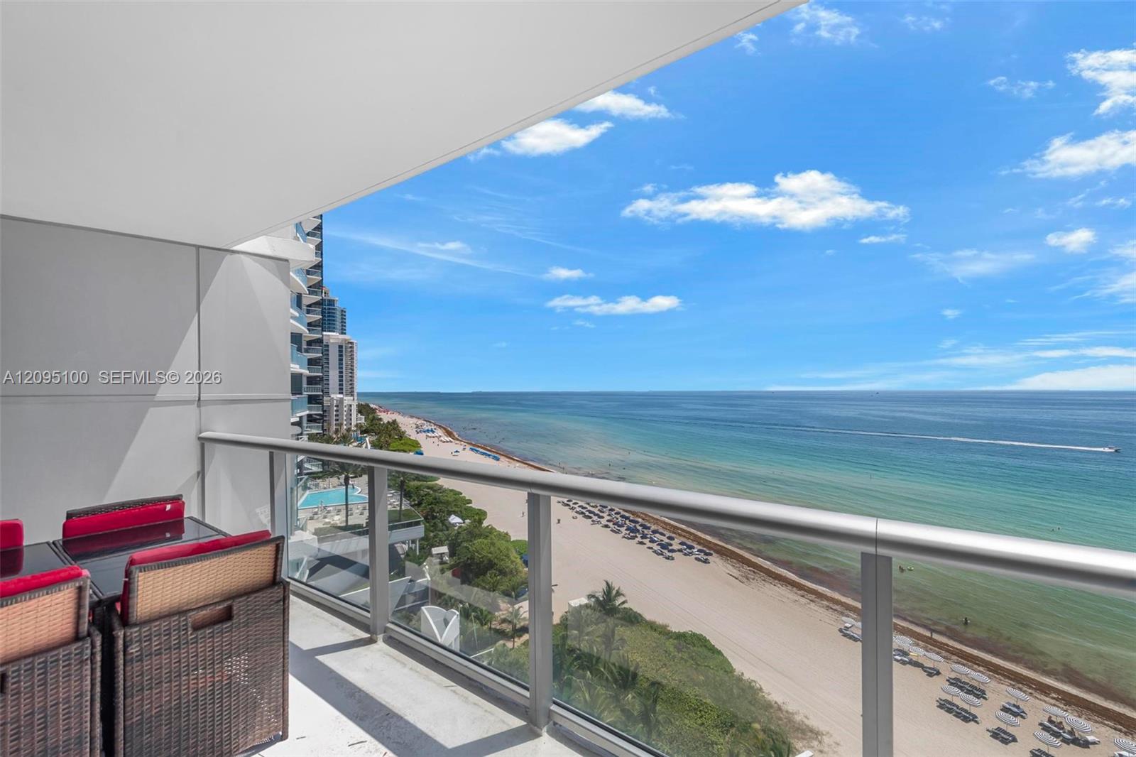 Furnished balcony overlooking a sandy beach and turquoise ocean, with neighboring beachfront towers along the coast.