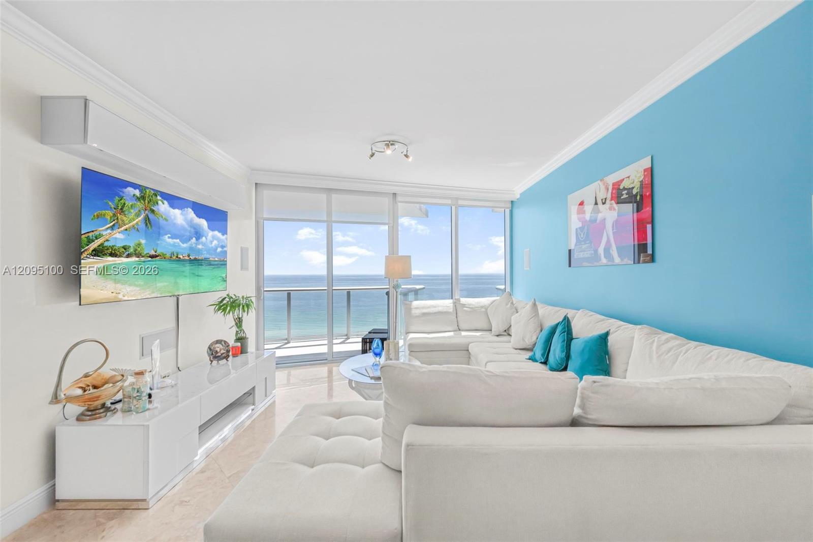 Furnished living room with a white sectional, turquoise wall, and ocean views through sliding glass doors.