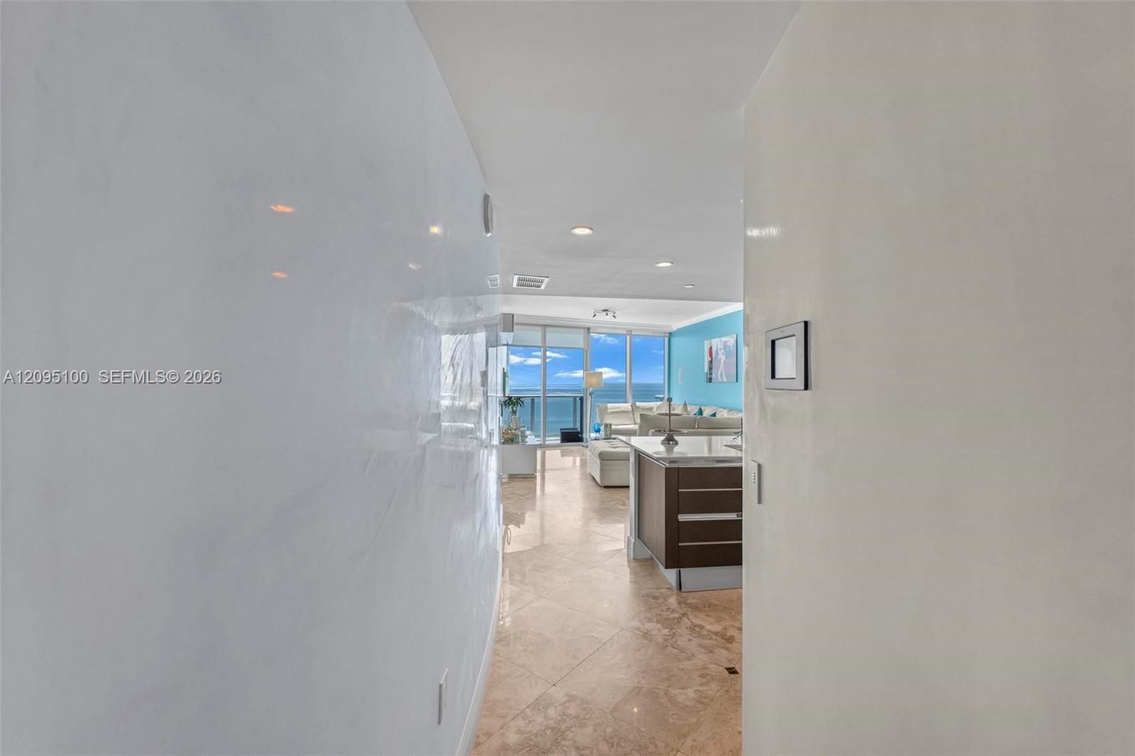 Hallway opening onto a furnished living room with floor-to-ceiling windows and an ocean view.