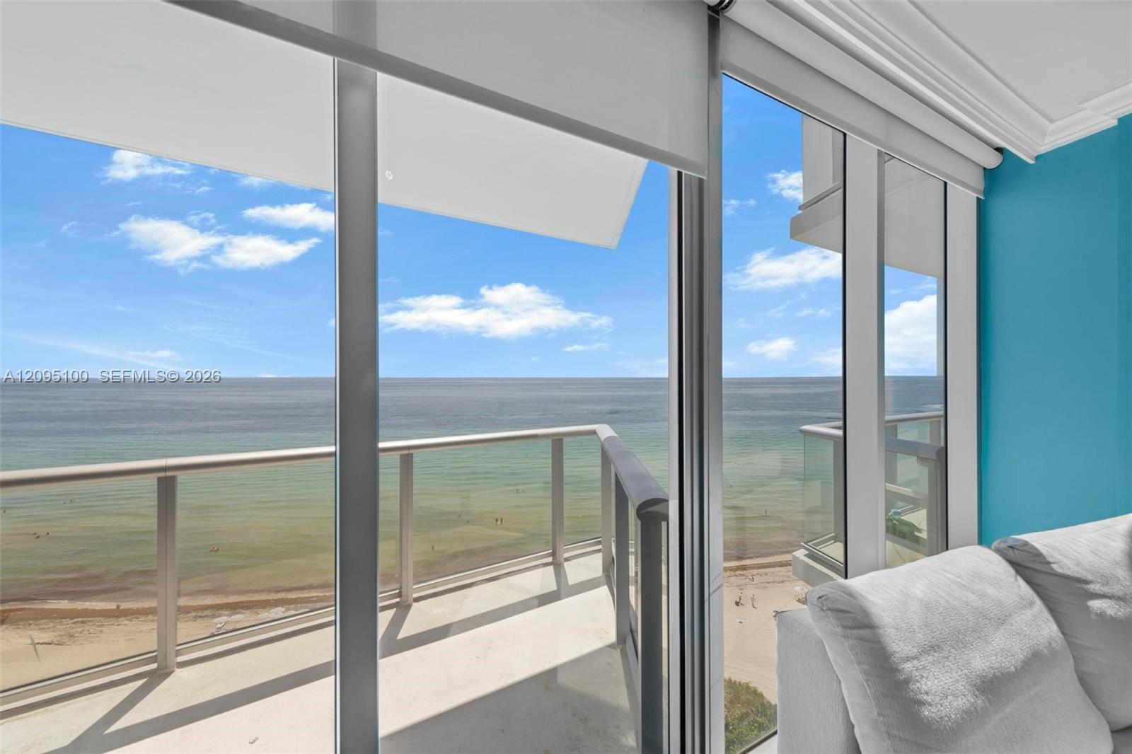 Condo living room with a balcony overlooking the ocean, framed by sliding glass doors and a gray sofa.
