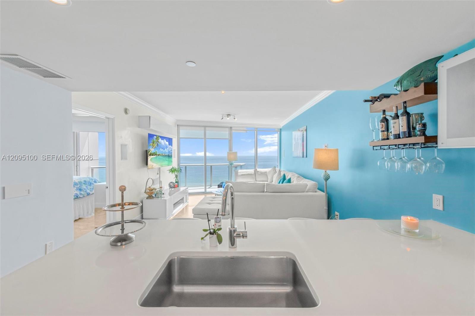 Furnished condo living room with turquoise accent wall and ocean views through floor-to-ceiling windows.