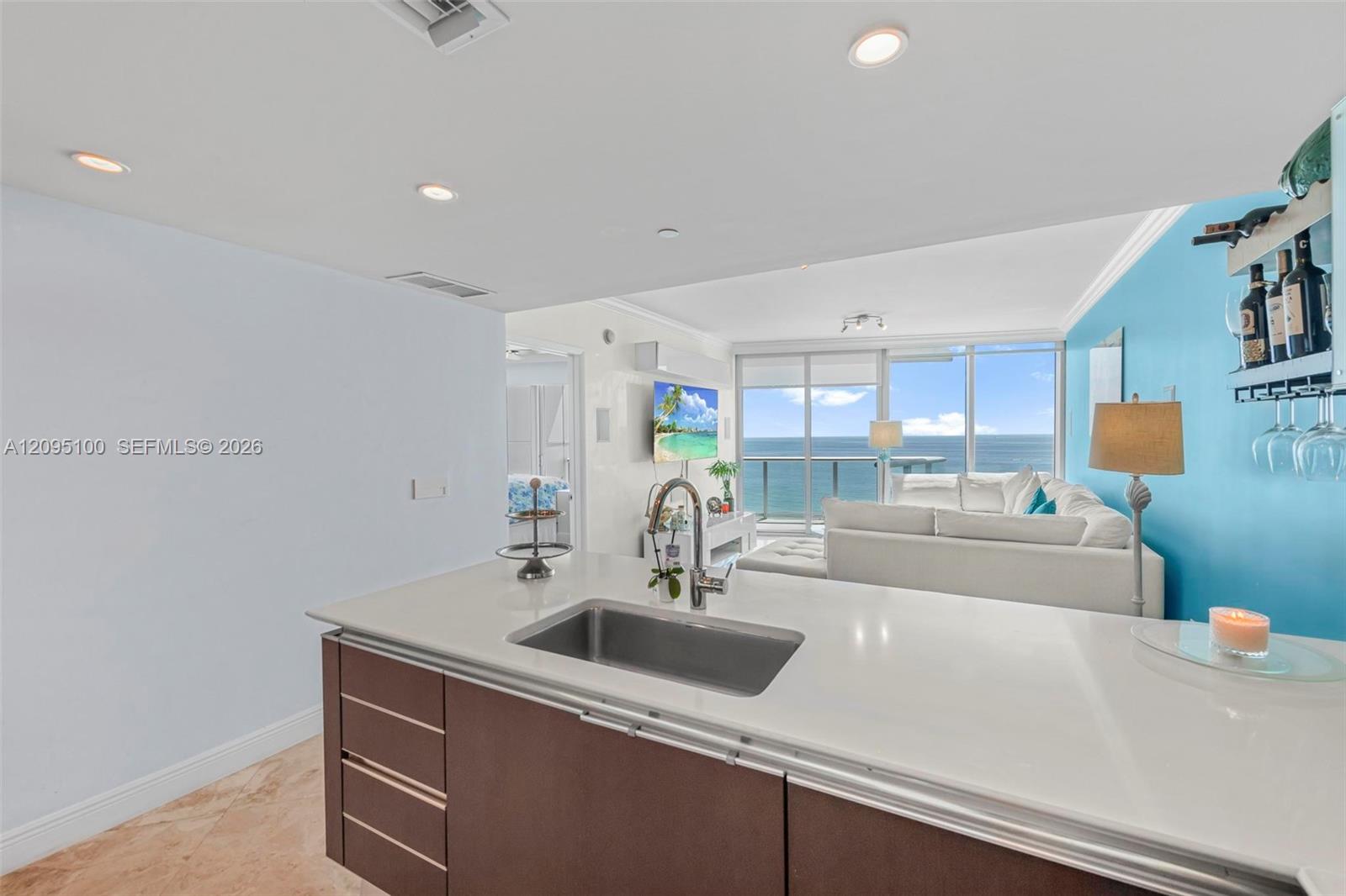 Condo kitchen and living room with an ocean view through floor-to-ceiling windows.