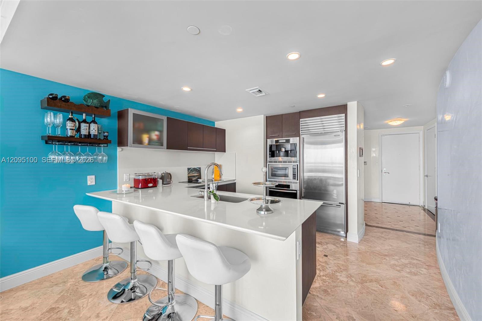 Modern kitchen with a large white island, three bar stools, stainless steel appliances, and a turquoise accent wall.