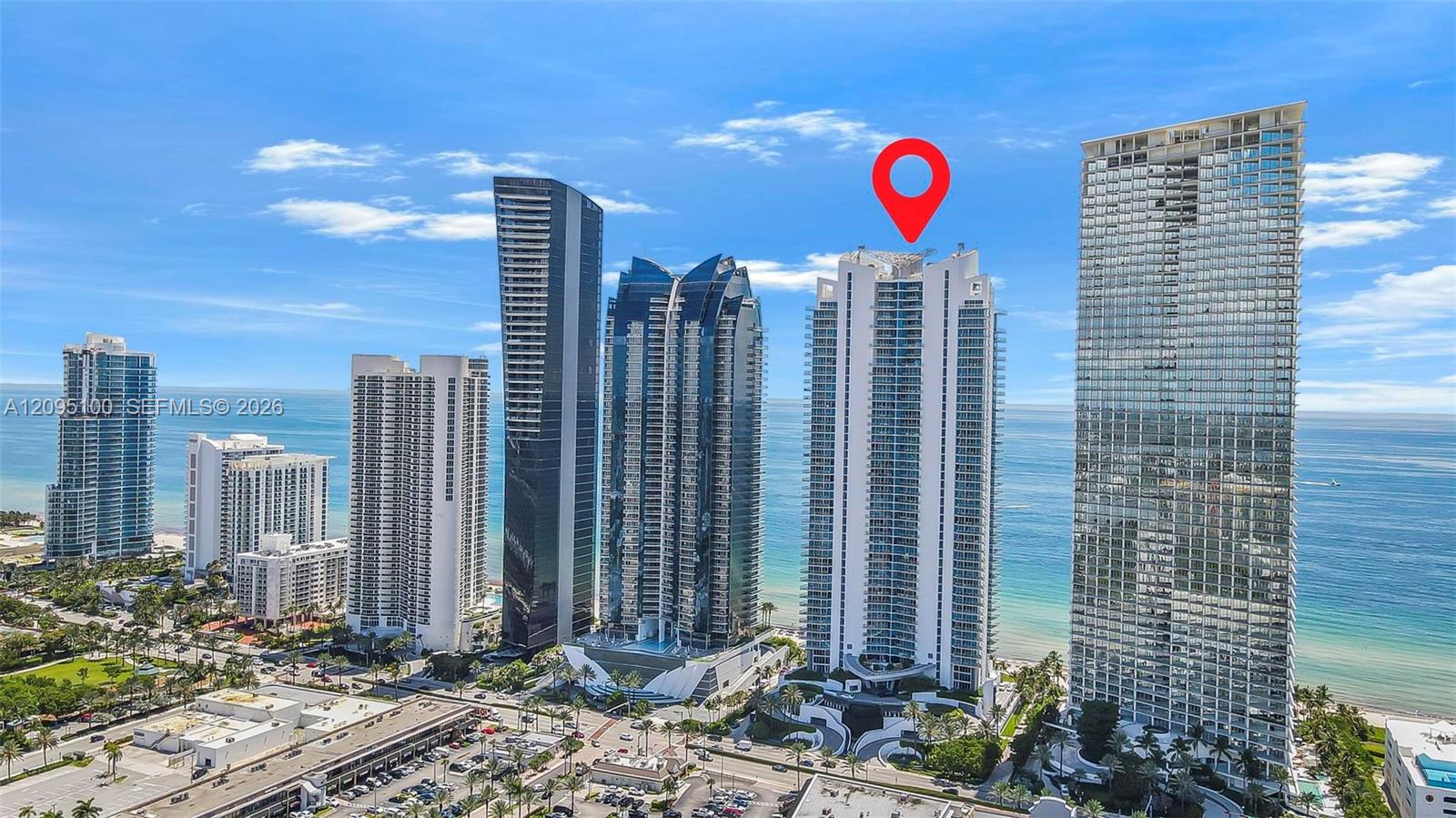 Aerial view of beachfront towers in Sunny Isles Beach, with a red pin marking a white high-rise.